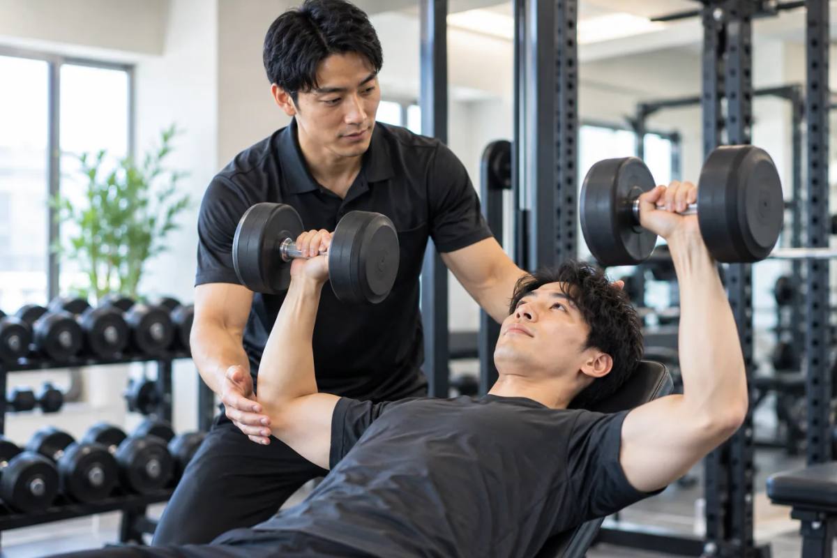 トレーナーの指導を受けながら正しいフォームで筋トレする男性