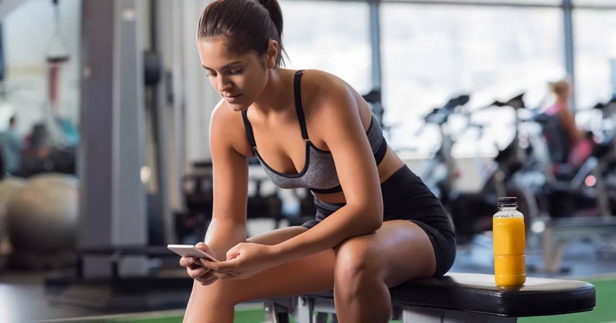 ジムのベンチに座りスマートフォンを見る女性