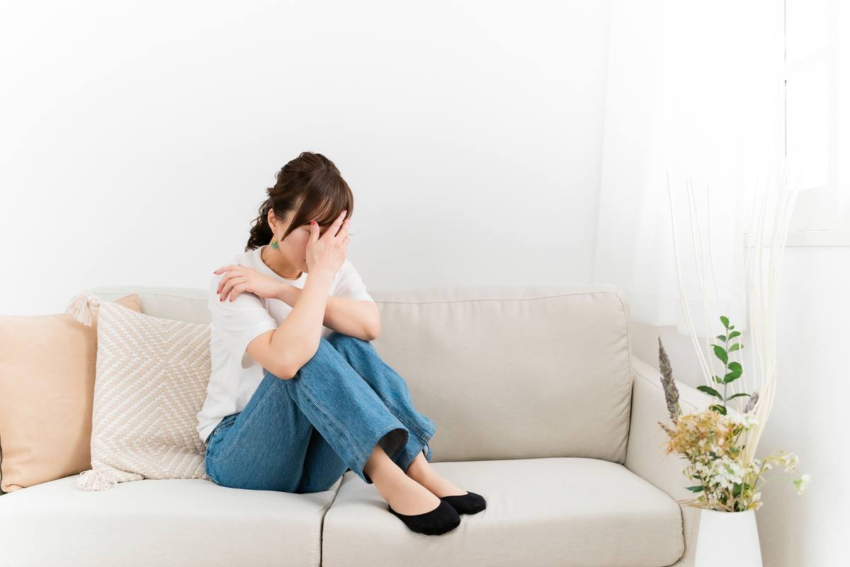 自宅のソファで膝を抱えてうつむく女性。通うのが止まってしまった状態のイメージ