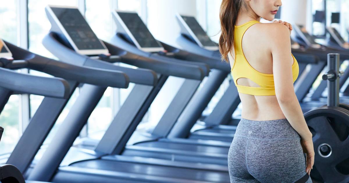 トレッドミルが並ぶジム内で走る黄色いトップスの女性の後ろ姿