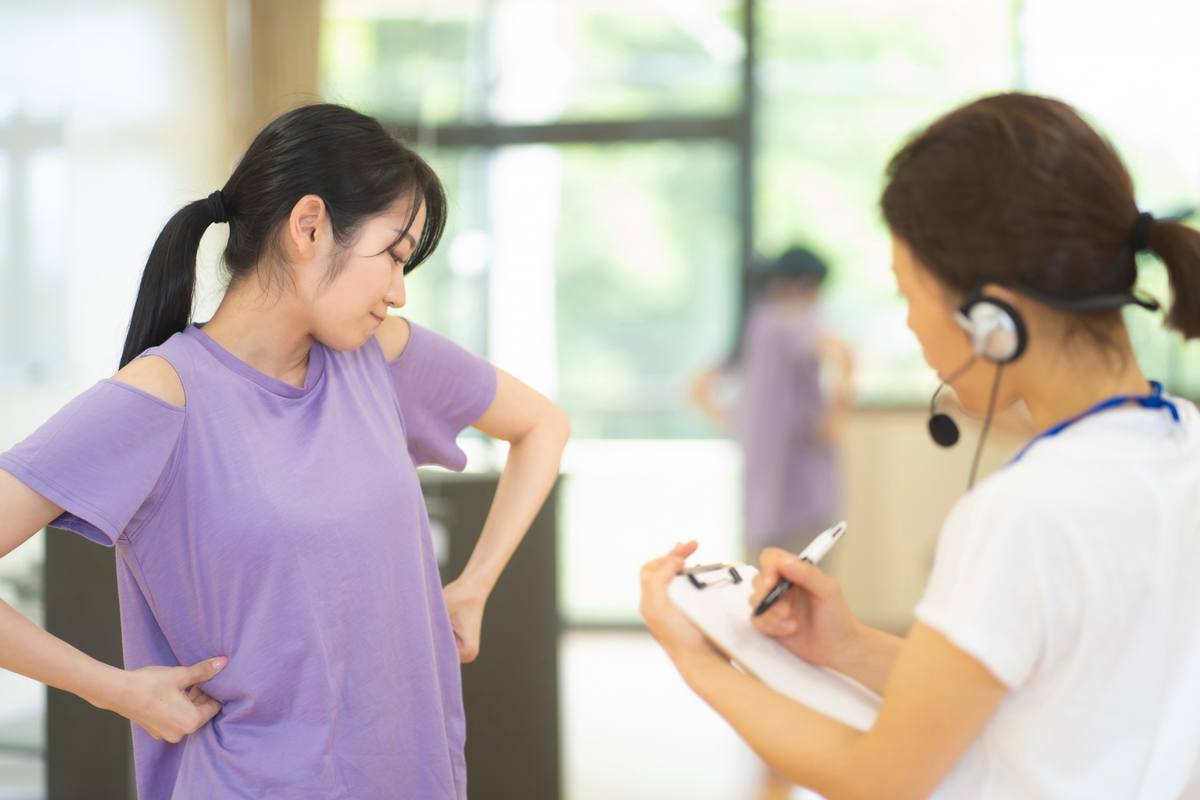 紫のウェアの女性にヘッドセットのスタッフがクリップボードで説明している様子