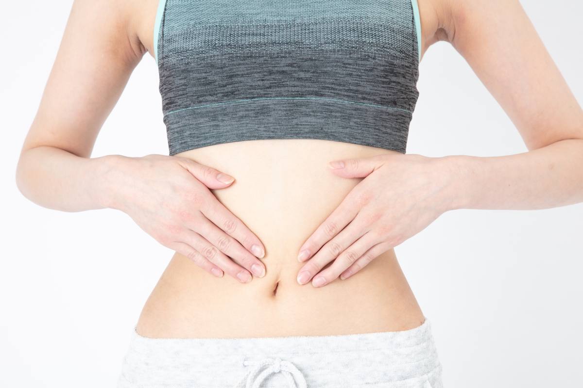 トレーニングウェア姿の女性が、両手を腹部に当てている様子