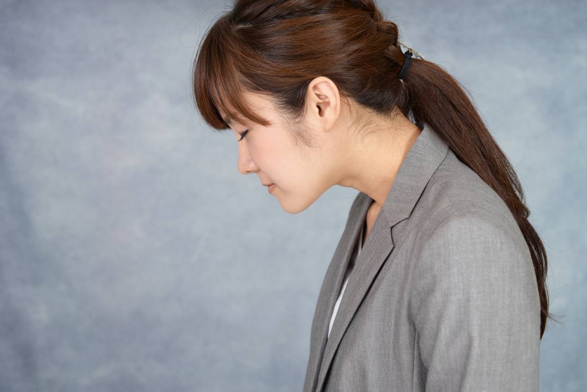 グレーのジャケットを着た女性が横を向き、うつむいて背中を丸めている様子