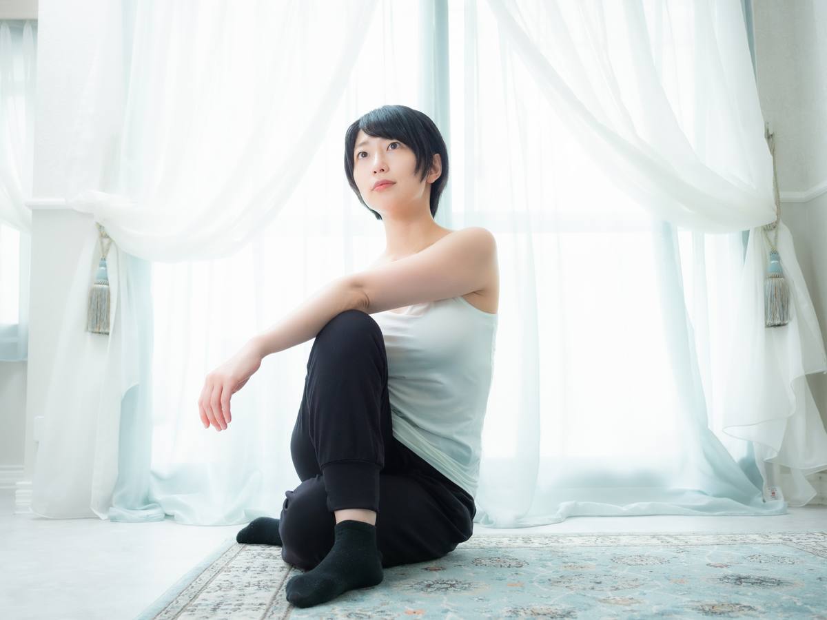 白いカーテンのある明るい部屋で、床に座って契約について考え込む女性