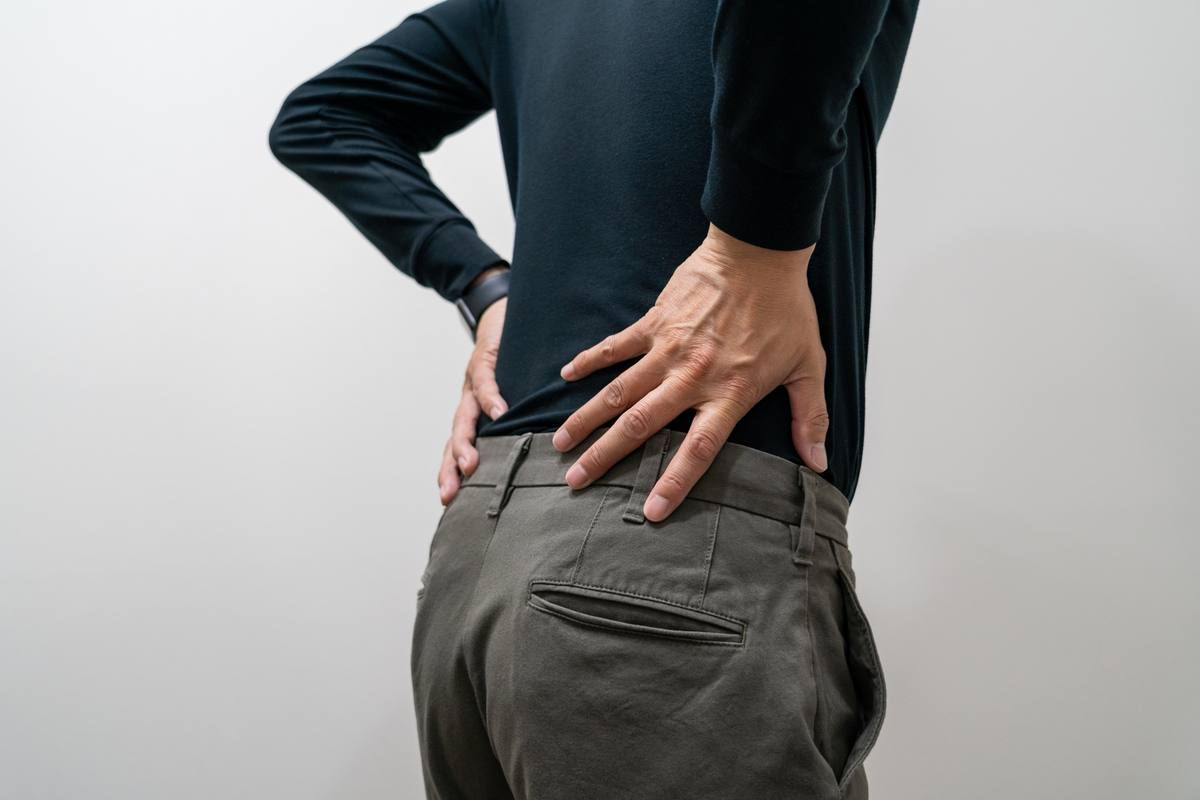 黒い長袖を着た男性が、両手を腰の後ろに当てて立っている様子