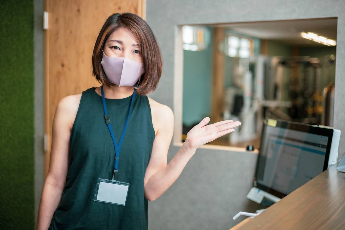 名札を着けたスタッフが受付付近で手のひらを上に向けて案内している様子