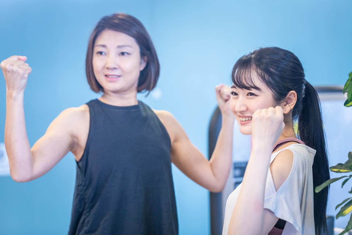 青い背景の前で2人の女性が笑顔でガッツポーズをしている様子